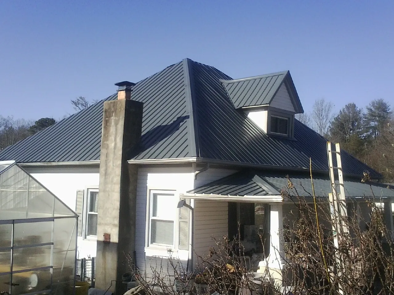 Dark blue standing seam metal roof on a white farmhouse with dormer — Slate & Tile Roof Repair by Roofing Brothers in Pheba