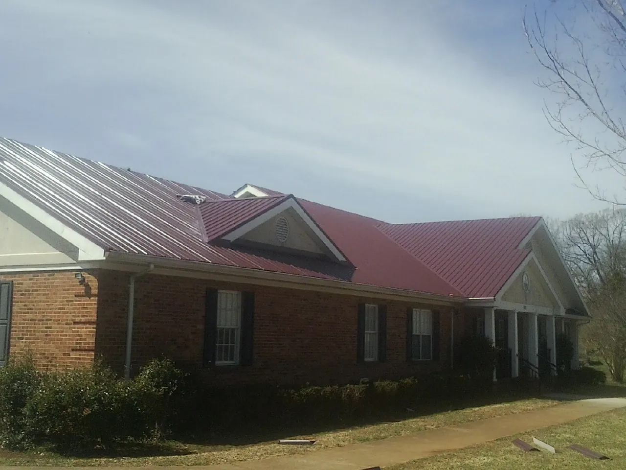 Red metal roof with gabled entries on a long brick building, from a Hail Damage Roof Repair job in Pheba