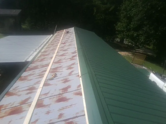 Old rusted panels beside newly installed green metal roofing — Wind Damage Roof Repair by Roofing Brothers in Pheba