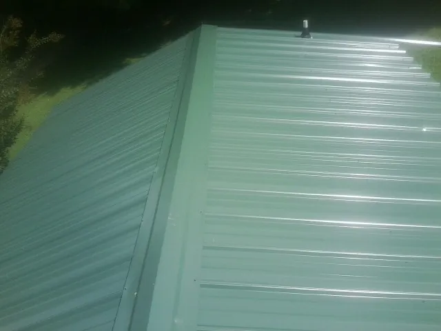 New green metal panels meeting at the ridge of a roof — Flat Roof Repair work by our crew in Pheba