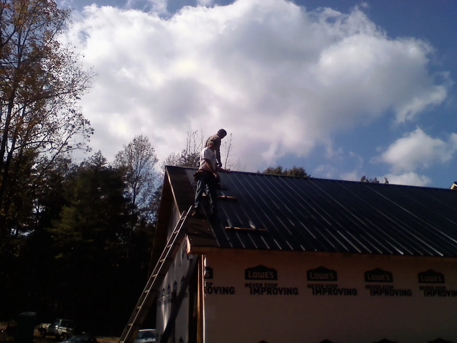 Roofer fastening dark metal panels high against a cloudy sky, from a Roof Inspection job in Pheba